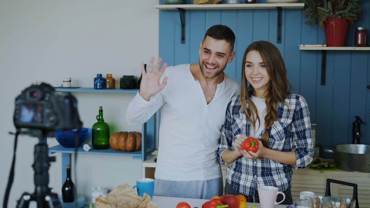 The Art of Drawing Readers In: Your attractive post title goes here Smiling couple filming a cooking vlog in a modern kitchen setting, engaging viewers.