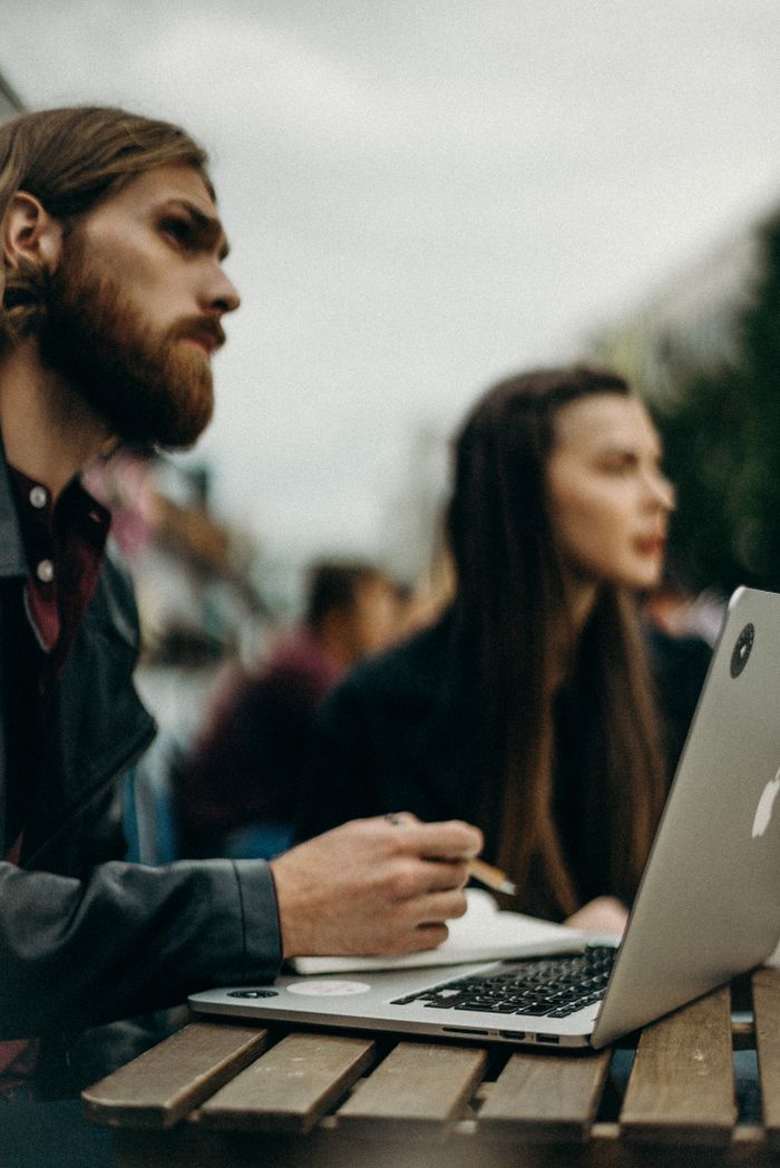 Portrait of young adults using laptops outdoors, focused on work and collaboration.